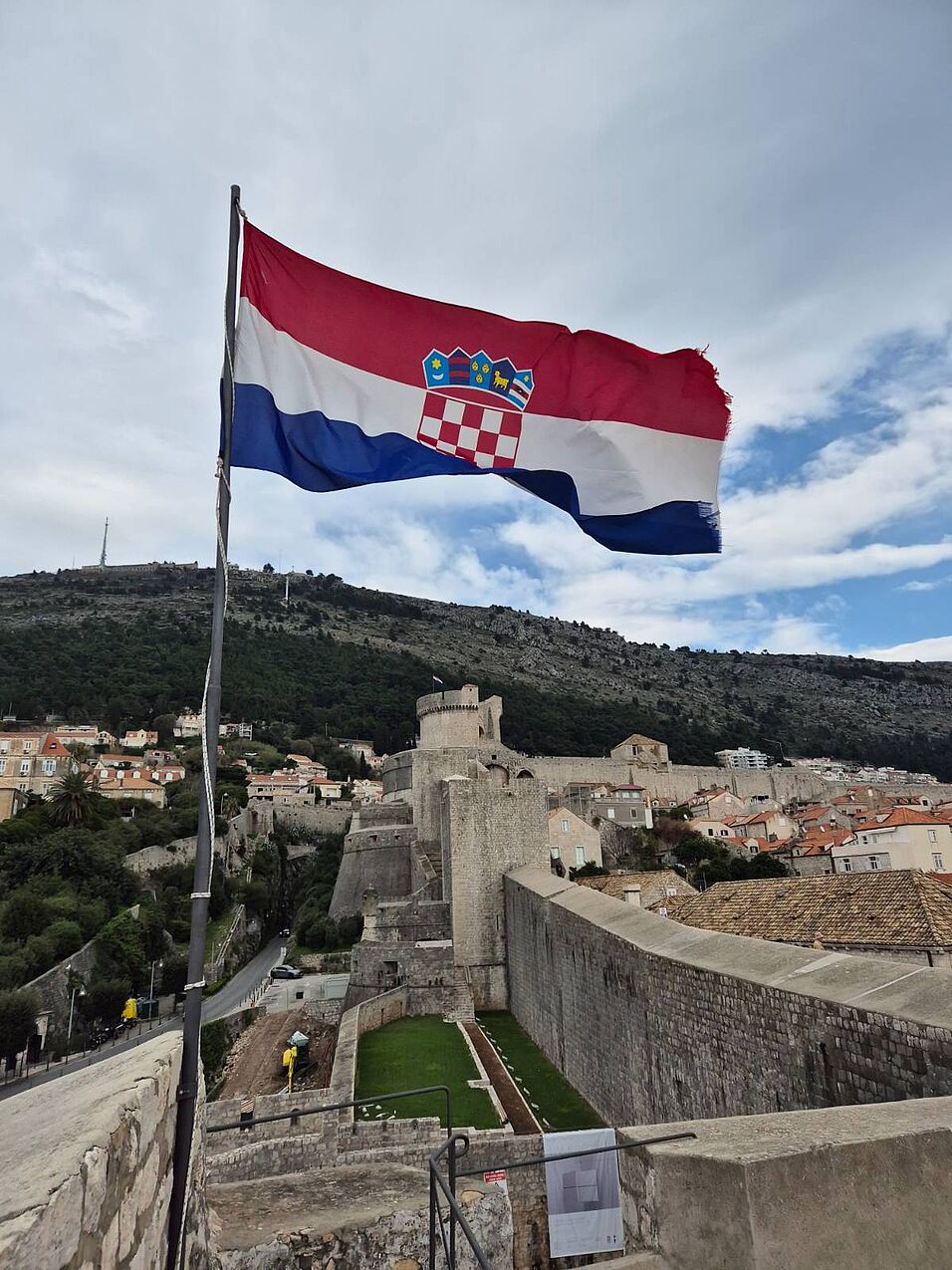 a Croatian flag waving in the wind; a hill and a historic fortress in the background